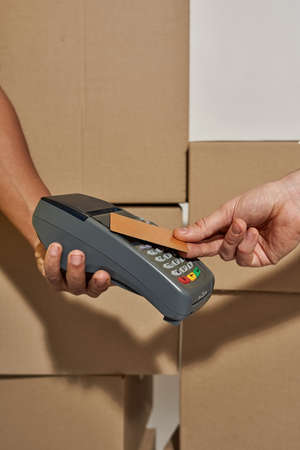 Close up shot of hands of delivery man holding terminal for a customer to pay for parcels received...