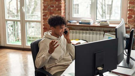 Relaxed young male trader making a call, discussing stock market while looking at charts, trading...