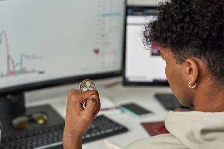 Close up of young male trader holding Ripple XRP crypto currency token, investing in stock market to exchange it while trading from homeの写真素材