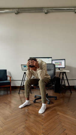 Hopeless young guy, trader holding head in despair after stock market business failure, sitting at desk, trading online from homeの写真素材