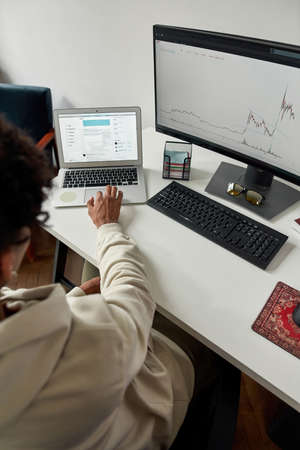 Rear view of young male trader using laptop and pc, looking at computer screen to analyze statistics...