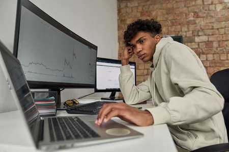 Portrait of young guy trader using online software to analyze price statistics and trading from home...