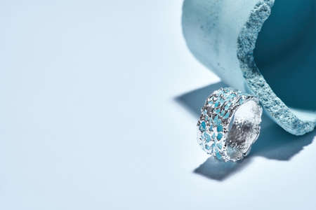 Macro shot of a ring made of silver metal with blue enamel arranged with industrial blue concrete...
