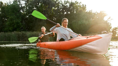 Motivated young couple of friends boating together on river with trees in the backgroundの写真素材