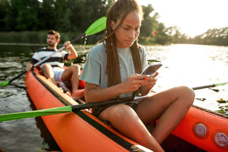 Portrait of young woman holding smartphone and texting while spending time with her boyfriend...