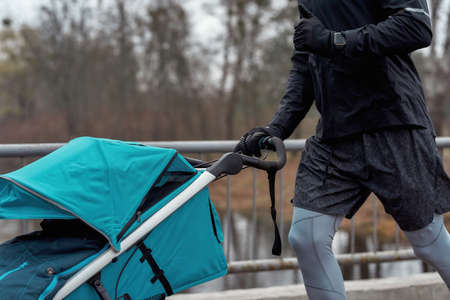 Close up shot of man in sportswear jogging with a stroller on a cold autumn day