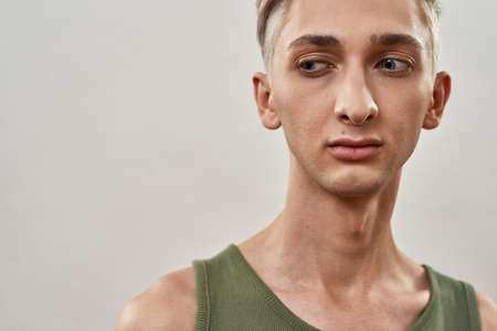 Portrait of androgynous transgender young man with makeup looking aside while posing isolated over light backgroundの写真素材