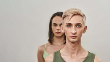 Couple of two young transgenders looking at camera, supporting, standing behind each other, posing together isolated over light backgroundの写真素材