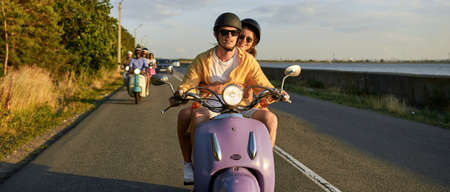 Romantic young couple riding moto scooter together with their friends, relaxing on weekend outside...