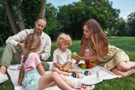 Happy family relaxing together outdoors, having picnic in nature on a summer day