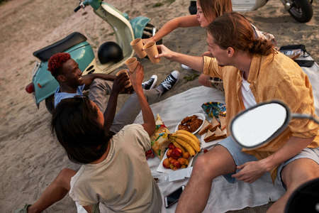 Group of young people enjoying picnic on the beach. Friends having summer party at sunset