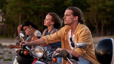 Caucasian young guy, motorcycle rider looking away, spending time together with his friends outside...