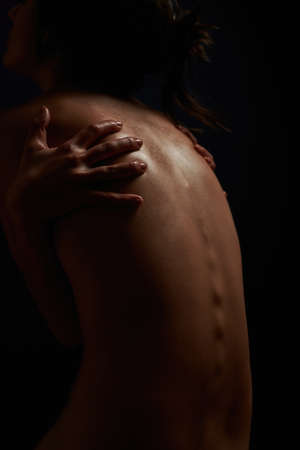 Silhouetted view of  back of young woman touching her body, posing isolated in darknessの写真素材