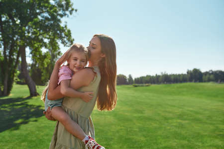 Caring young mother holding her tired little daughter while spending time together in summer parkの写真素材