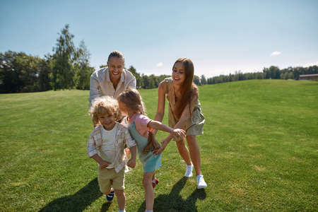Active parents with two little kids playing catch together in green park on a summer day. Happy family enjoying leisure activityの写真素材