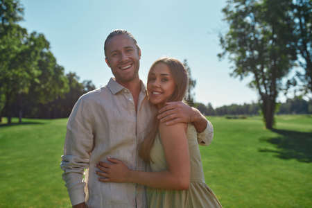 Portrait of cute young couple smiling at camera, posing together outdoors while standing in the park