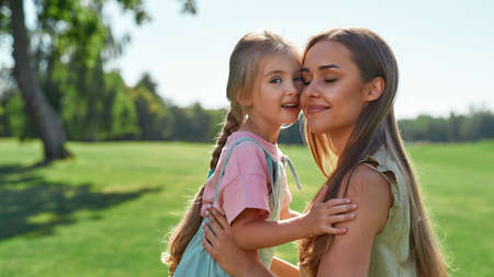 Portrait of happy young mother embracing her cute little daughter, smiling with eyes closed while...