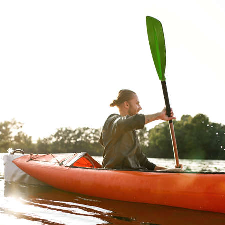 Young man kayaking on river, holding paddle, looking away on a summer dayの写真素材