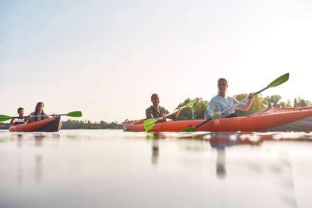 Young adventurous friends looking cheerful while kayaking in a river surrounded by the beautiful nature on a summer dayの写真素材