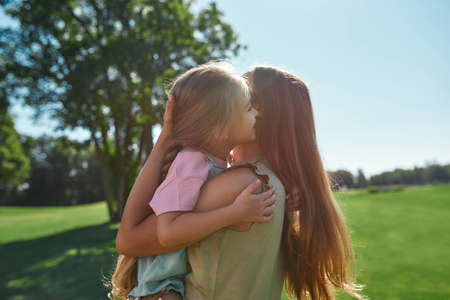 Loving mother playing with her cute little daughter, holding her while spending time together in summer parkの写真素材