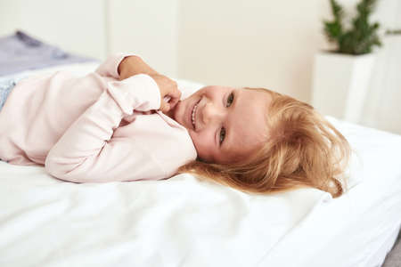 Happy little girl kid relax on bed at homeの写真素材