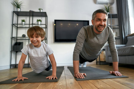 Smiling active dad and son exercise train together at homeの写真素材