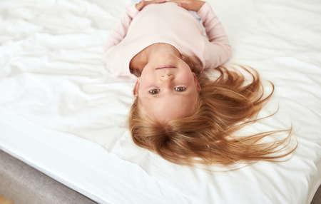 Portrait of cute little girl lying on bed at homeの写真素材