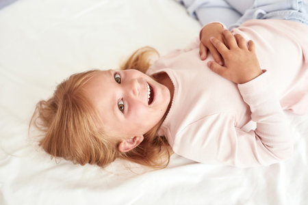Smiling little girl child relax on cozy bed at homeの写真素材