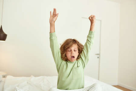 Teen boy stretch wake up in bed in morningの写真素材