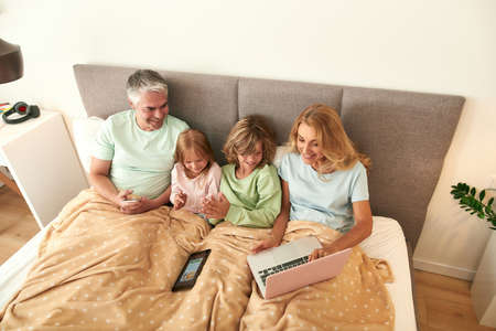 Smiling family stay in bed on quarantine use laptop