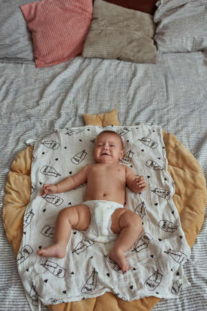Crying baby on large bed, top view