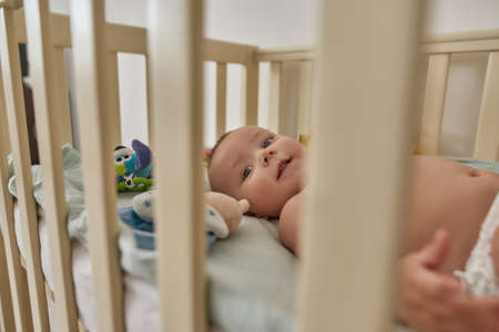 Cheerful baby looking at camera through crib barsの写真素材
