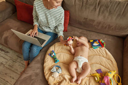 Playful baby and working mother at home during quarantineの写真素材