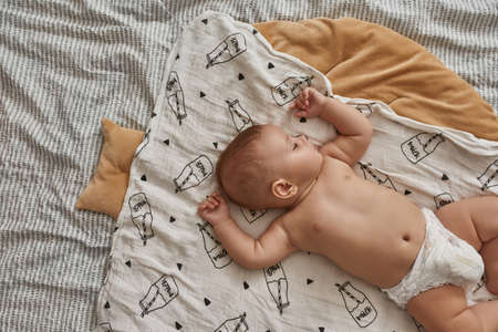 Undressed infant baby sleeping in bed on cosy comforterの写真素材