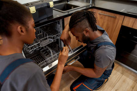 Female apprentice helping handyman to fix dishwashing machineの写真素材