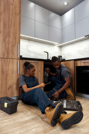 Two diverse technicians doing kitchen sink preventive maintenanceの写真素材