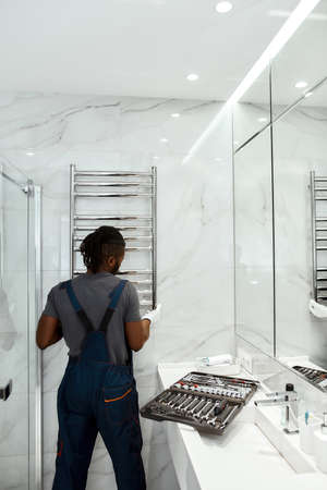 Young plumber installing electric towel rail in modern bathroomの写真素材