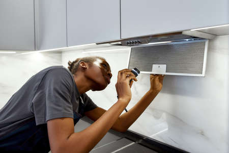 Female worker repairing modern cooker hood, holding flashlight in kitchenの写真素材