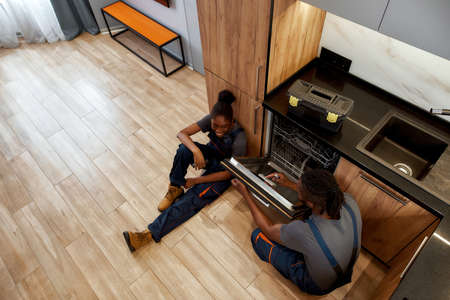 Woman and man in workwear happily chatting, sitting on kitchen floorの写真素材