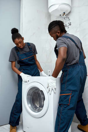 Young African American couple of technicians setting up washing machineの写真素材