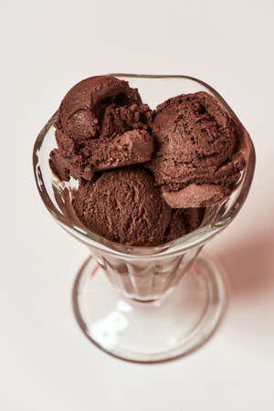 Top view of scoops of tasty chocolate ice cream in a glass sundae dish isolated over light...