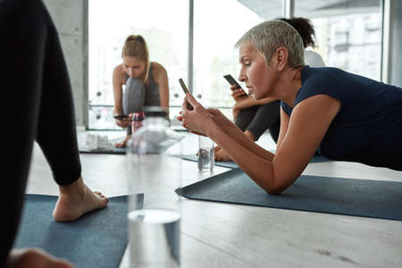 Middle-aged woman use cellphone at training workout in gymの写真素材