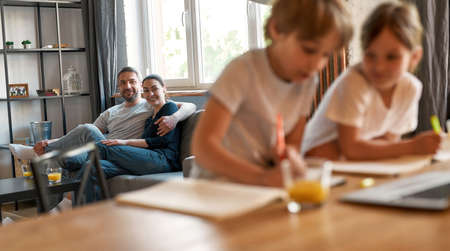 Smiling couple parents watch kids studying alone