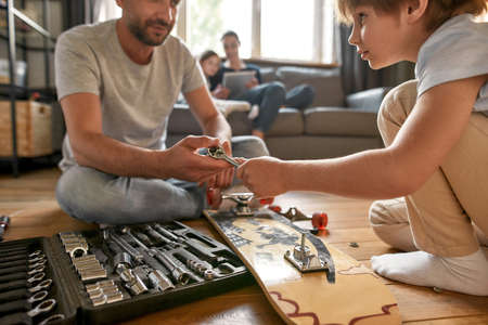 Close up father and teen son repair skateboard with toolsの写真素材