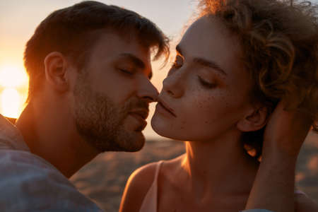 Portrait of young people in love looking passionate, kissing each other on the beach at sunsetの写真素材