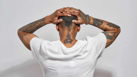 Back view of tattooed head, neck and arms of young dark skinned man posing isolated over white backgroundの写真素材
