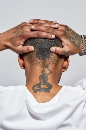 Back view of shaved tattooed head and neck of young dark skinned man posing isolated over white...