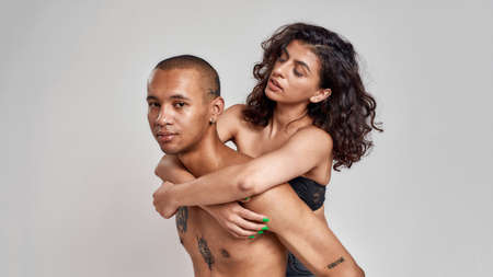 Beautiful young people, tattooed guy and his girlfriend with curly dark hair posing half naked together isolated over gray backgroundの写真素材