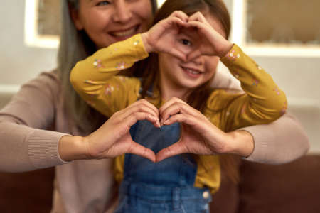 Childhood, love and care concept. Female and childs hands showing heart sign