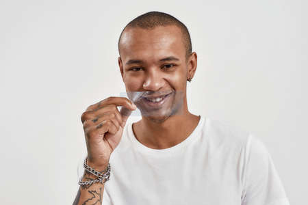 Playful mixed race guy holding blue film in front of his mouth, smiling at camera, posing isolated over white backgroundの写真素材